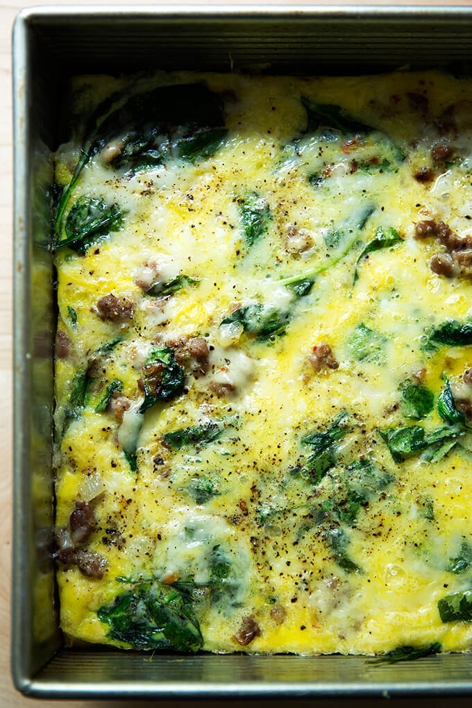 An up-close shot of a breakfast casserole with eggs, Gruyere, sausage, spinach, and onions.