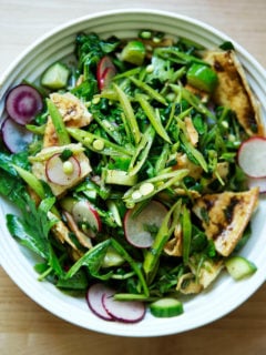 A bowl filled with a spring fattoush salad with arugula, radishes, snap peas, and cucumbers.