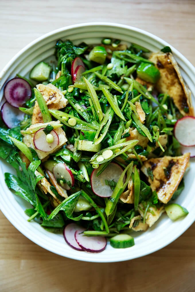 A bowl filled with a spring fattoush salad with arugula, radishes, snap peas, and cucumbers.