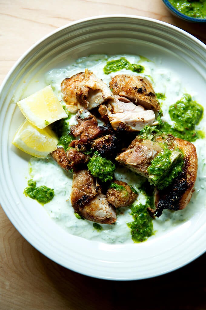 A platter of grilled, smokey chicken, cucumber-yogurt sauce,, skhug and lemon