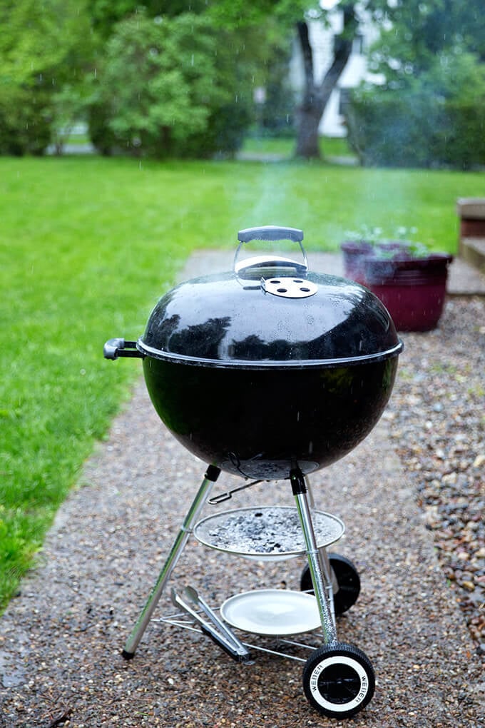 A weber grill with hot coals in the rain.