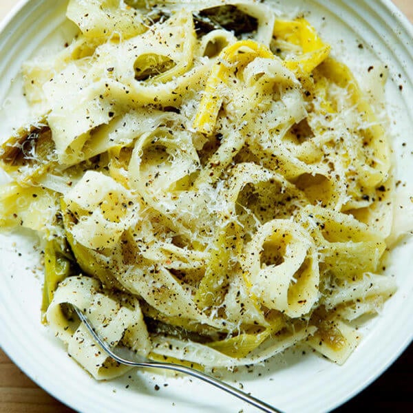 A bowl of braised leek pappardelle with a fork and grated parmesan over top.