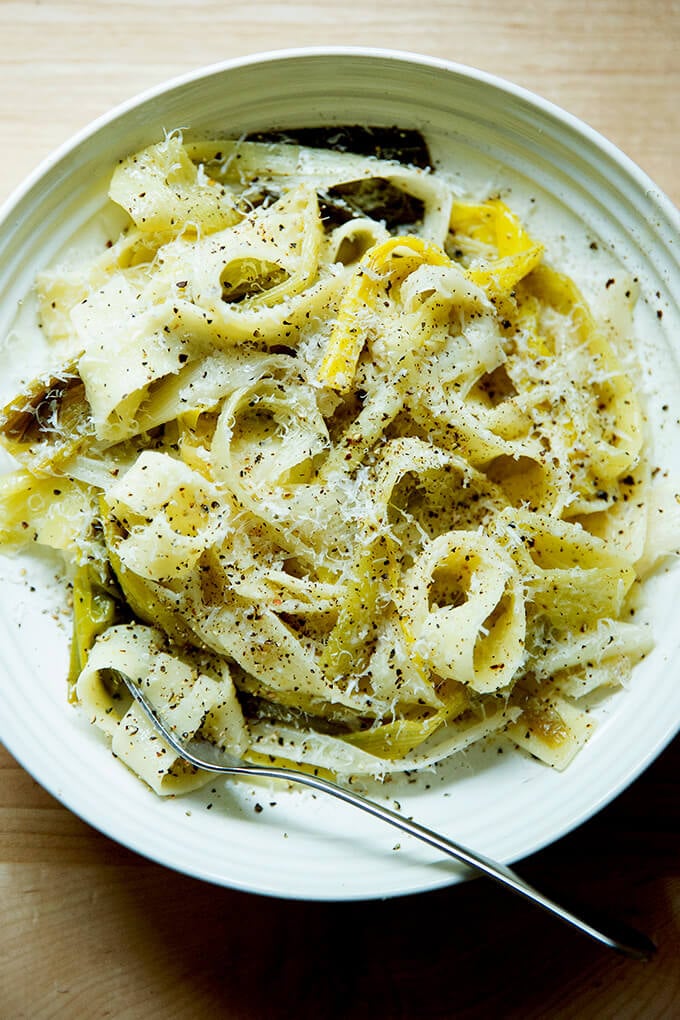 A bowl of braised leek pappardelle with a fork and grated parmesan over top.