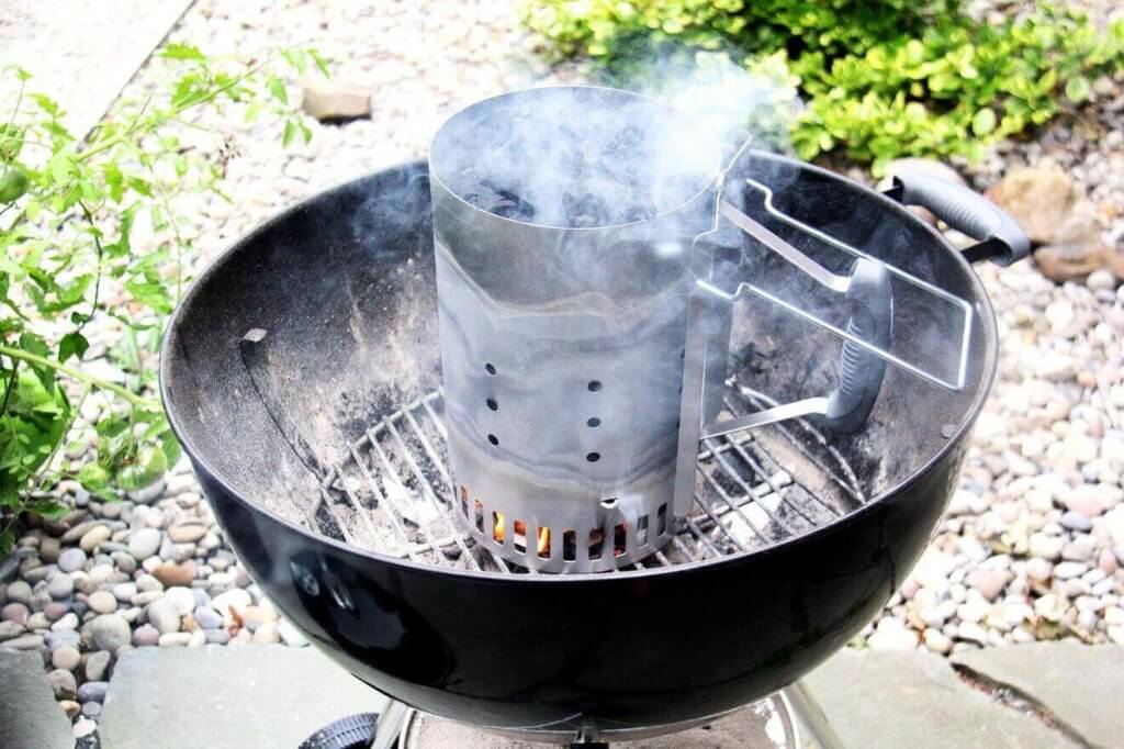 A charcoal Weber grill with a chimney starter holding burning coals inside.