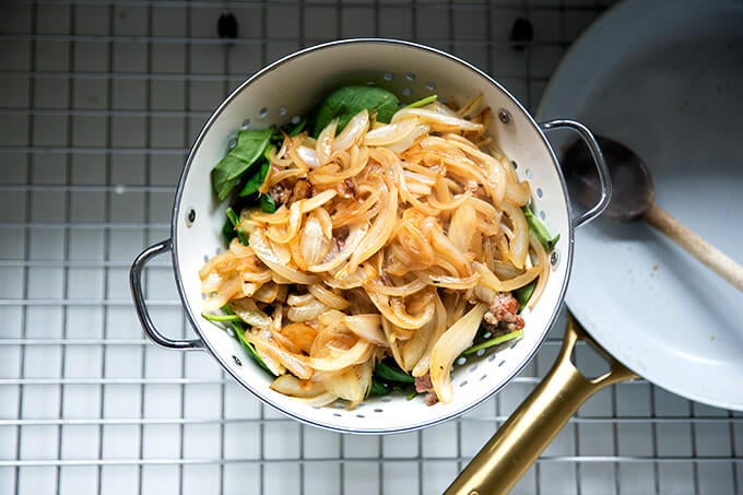 Caramelized onion on top of sausage and spinach in colander in sink.