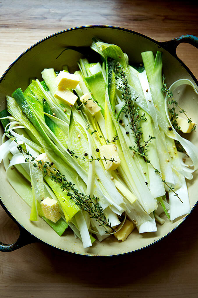 A braising pan filled with leeks, butter, water, wine, and seasonings.