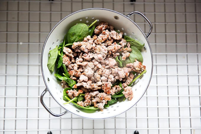 Sausage and spinach in colander in sink.