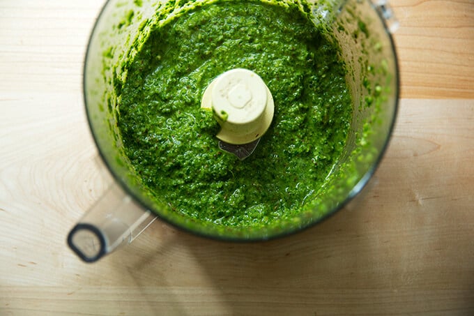 a food processor filled with skug, an herby, spiced sauce with parsley, cilantro, cumin, coriander, garlic, jalapenos, olive oil and lemon