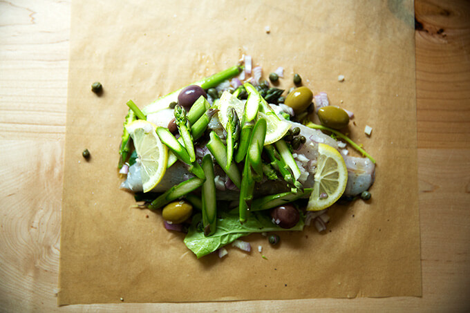 a parchment paper with Swiss chard, Branzino, capers, and olives.
