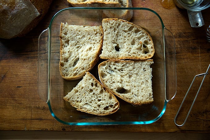 Slices of sourdough soaking in olive oil and vinegar in a square 8-inch pan.