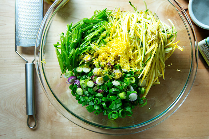 A bowl with slivered snap peas, summer squash, spring onions, lemon zest.