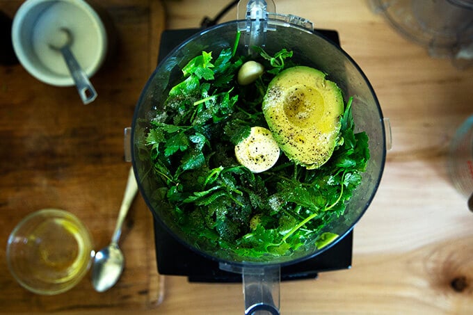 A food processor holding the ingredients to make the green sauce.