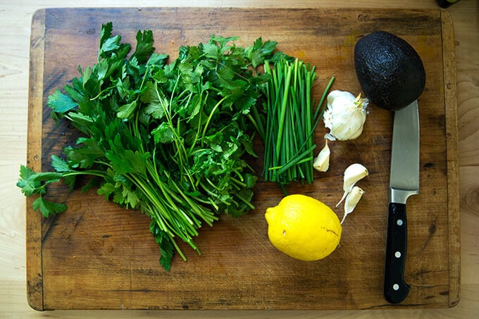 A cutting board with the ingredients to make a green sauce.