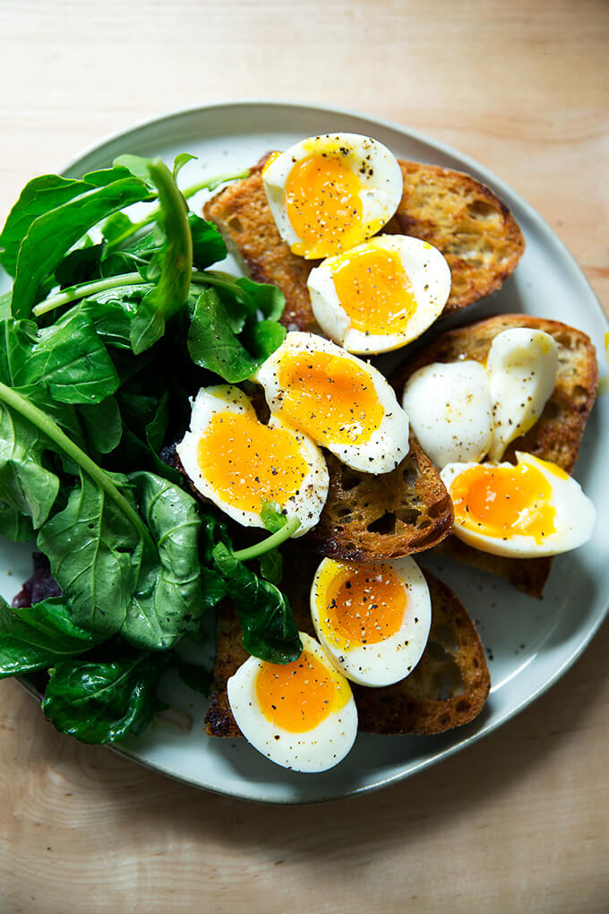 A plate of vinaigrette toasts topped with soft-boiled eggs aside dressed arugula.