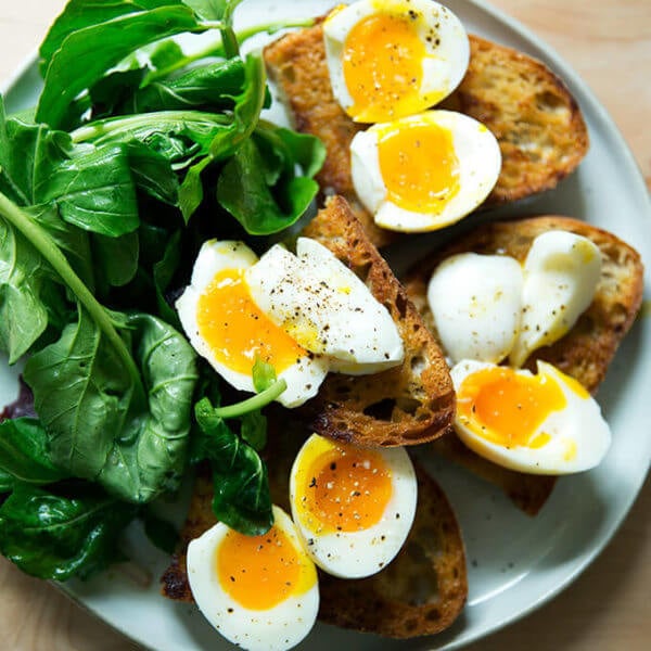 A plate of vinaigrette toasts topped with soft-boiled eggs aside dressed arugula.