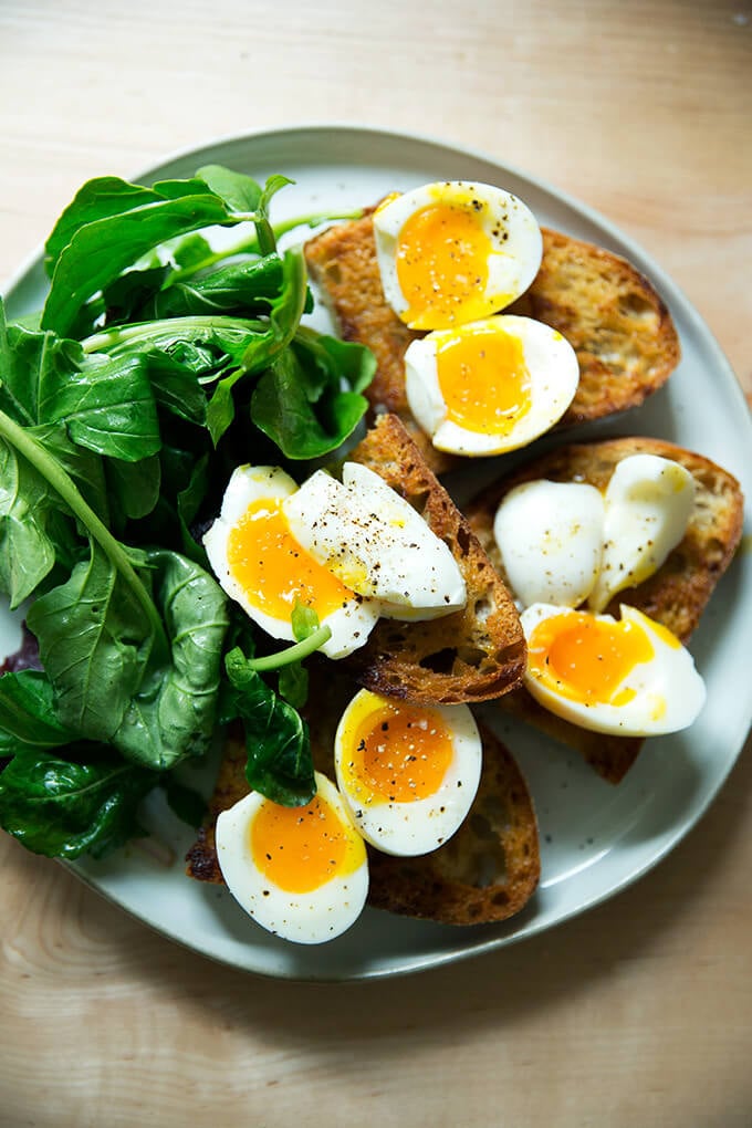 A plate of vinaigrette toasts topped with soft-boiled eggs aside dressed arugula.