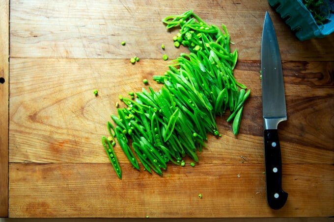 A cutting board with slivered snap peas. 