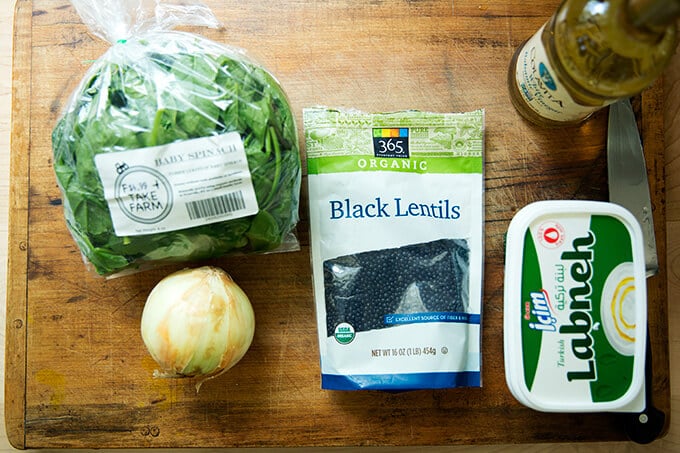 A cutting board with the ingredients to make black lentils with spinach.