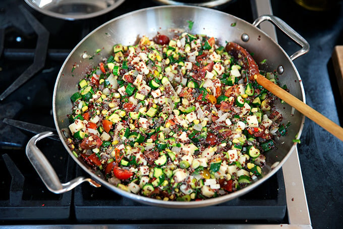 A sauté pan filled with corn, zucchini, tomatoes, and quinoa.