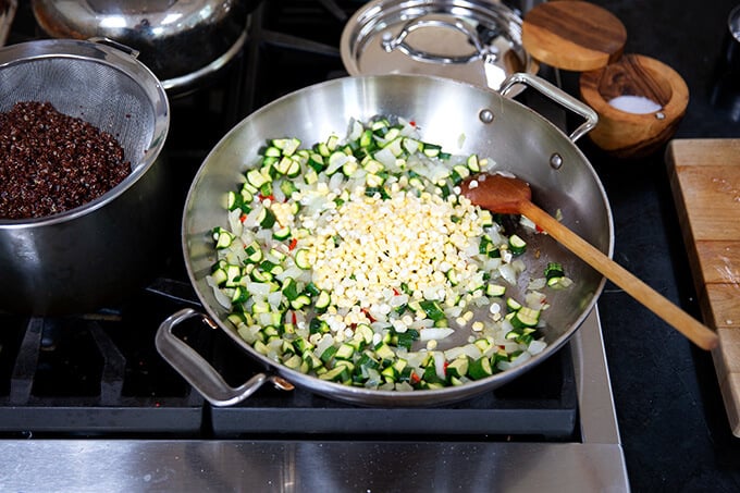 A sauté pan filled with onions, chili, zucchini, and corn.