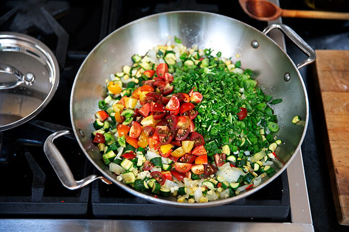 A sauté pan filled with onions, chili, zucchini, corn, tomatoes, and herbs. 