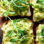 Four slices of sourdough bread topped with avocado egg salad and sprouts.