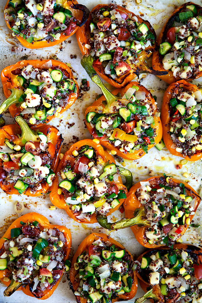A sheet pan of orange bell peppers stuffed with quinoa, vegetables, and Monterey Jack cheese.