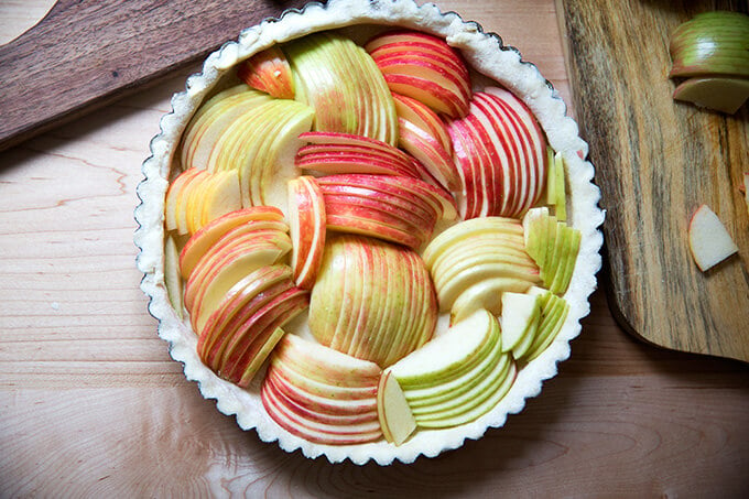 An unbaked French apple tart shell filled with sliced apples.