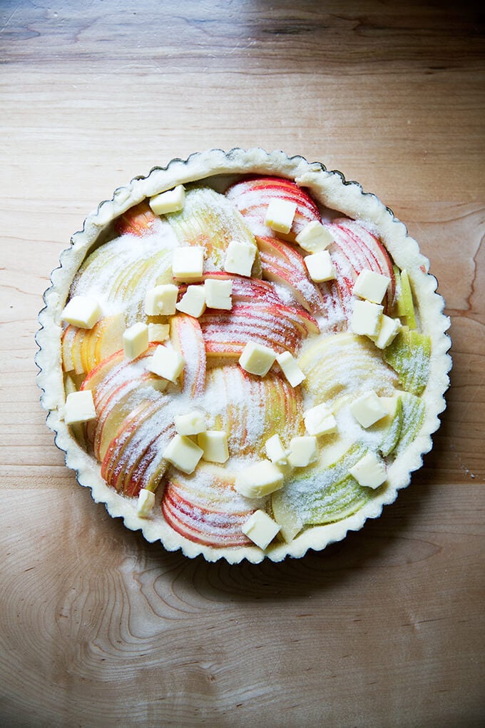 An unbaked French apple tart covered in sugar and butter.