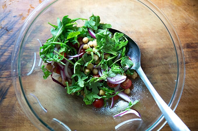 A large bowl of chickpeas, tomatoes, red onions, and arugula.