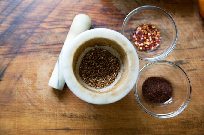 A mortar and pestle with crushed spices aside bowls of more spices.