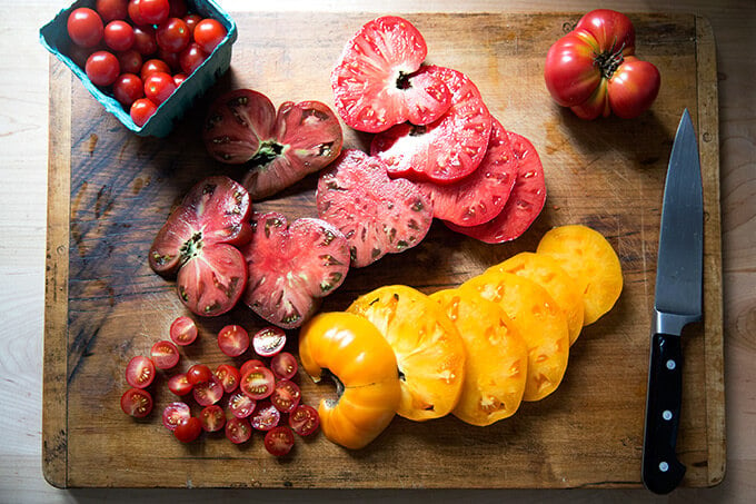 A large cutting board with sliced tomatoes on top.