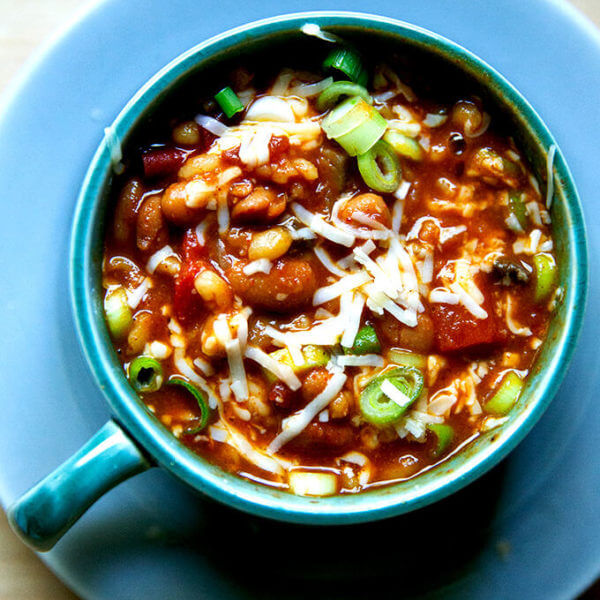 A bowl of spicy, smoky stovetop vegetarian chili with cheese and scallions stirred in.