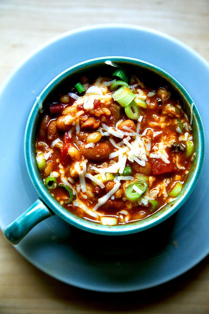 A bowl of spicy, smoky stovetop vegetarian chili with cheese and scallions stirred in.