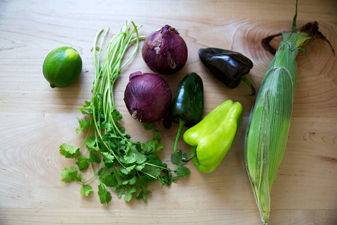 vegetables on a countertop: lime, cilantro, onions, poblano peppers, and corn