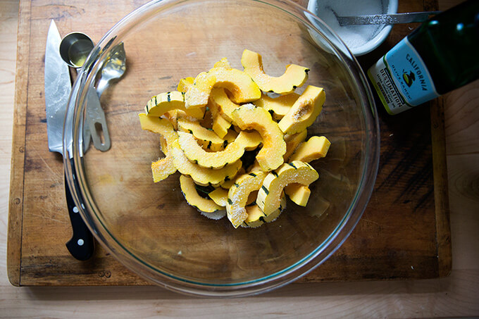 A large bowl filled with cut delicata squash slices, olive oil, and salt. 