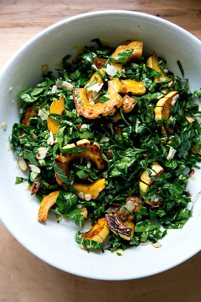 A large bowl filled with raw collard greens salad tossed with roasted delicata squash. 