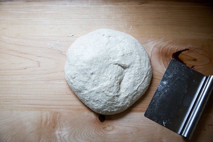 A blob of sourdough on the counter aside a bench scraper.