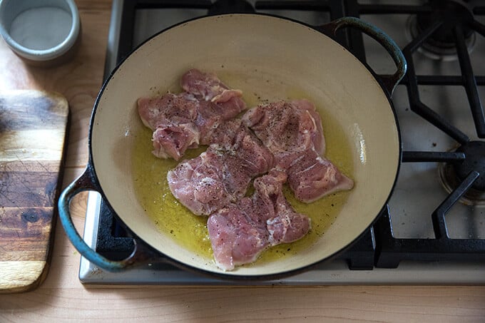 A skillet with olive oil and 4 chicken thighs browning.