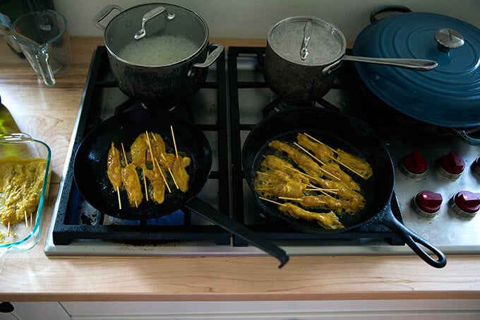 Two cast iron skillets on a stovetop cooking easy Thai chicken satay.