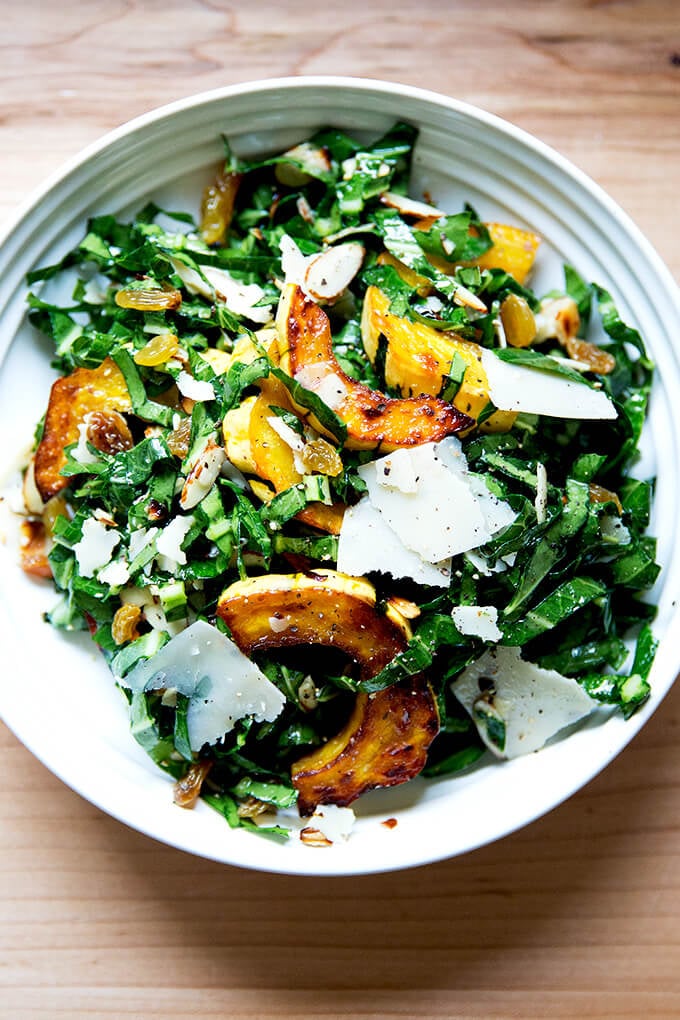 A bowl of raw collard greens salad with roasted delicata squash, golden raisins, shaved parmesan, and toasted almonds.