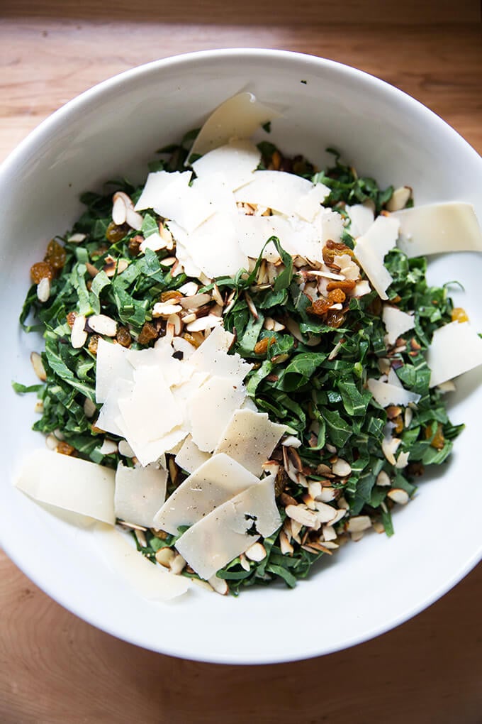 A bowl of shaved collard greens, almonds, golden raisins, and shaved parmesan. 