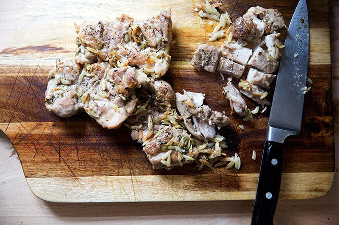 A board with 4 cooked chicken thighs being cut into cubes. 
