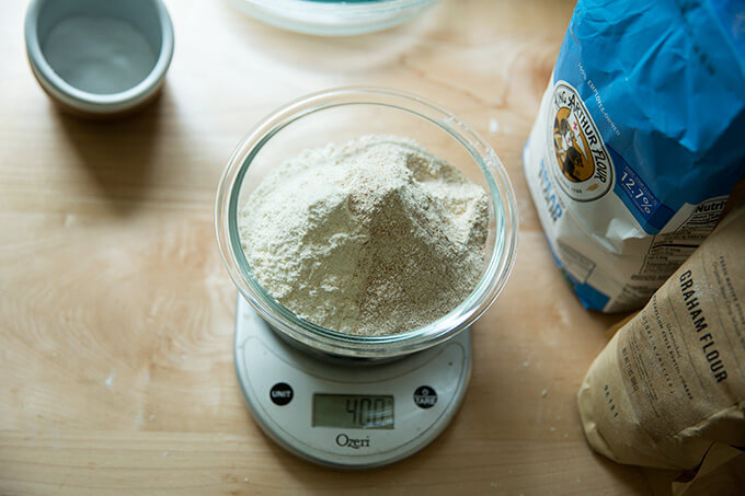 A bowl on a scale filled with bread flour, graham flour, and rye flour.