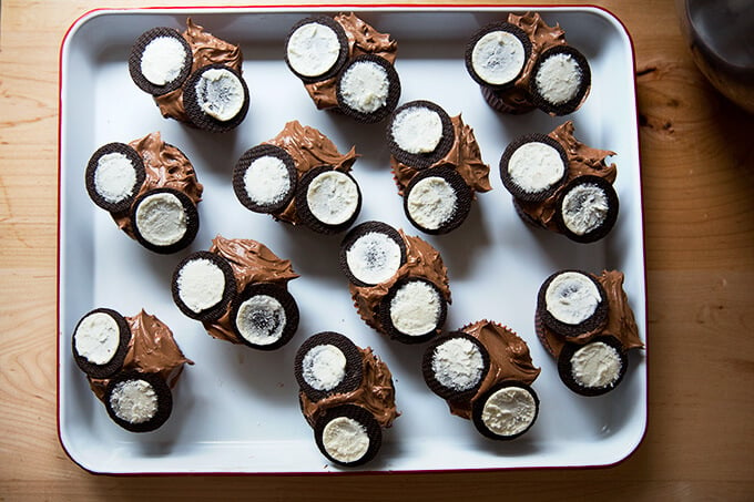 A tray filled with chocolate frosted cupcakes each topped with two Oreo halves. 