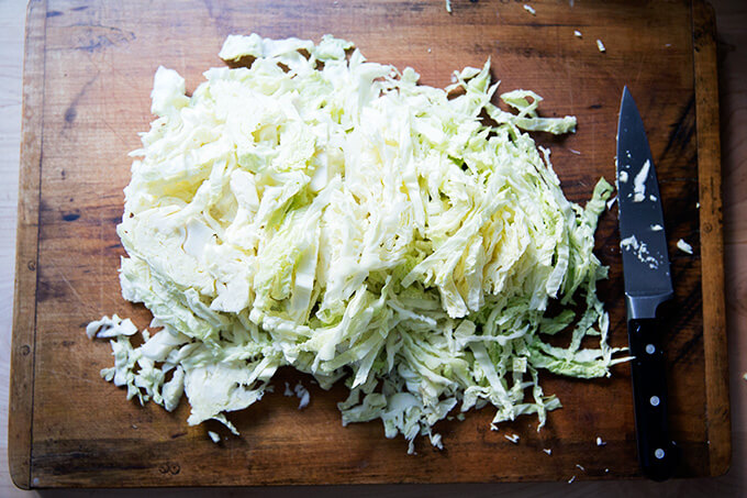 An overhead shot of a board with a head of cabbage finely shredded on top. 