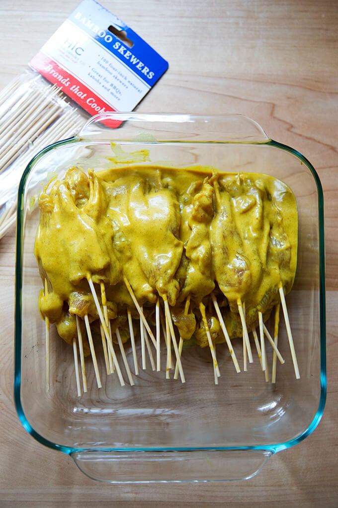 A square glass pan holding skewers of easy Thai chicken satay.