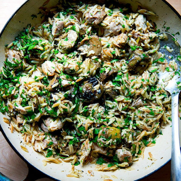 An over head shot of a skillet holding one-pan lemon chicken orzo with artichoke hearts.