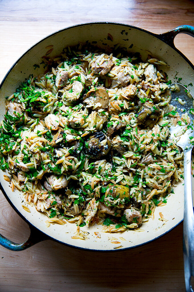 An over head shot of a skillet holding one-pan lemon chicken orzo with artichoke hearts.