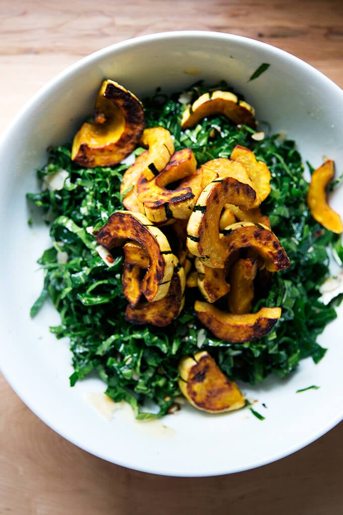 A bowl of raw collard greens salad topped with roasted delicata squash. 